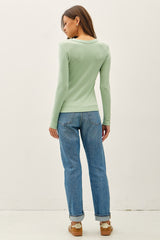 woman wearing a light green long sleeve top and blue high-waisted jeans, seen from the back