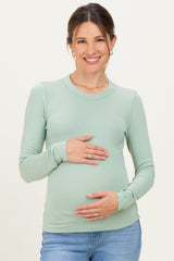 woman wearing a light green long sleeve maternity top and holding her baby bump