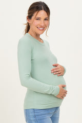 woman wearing a light green long sleeve maternity top and holding her baby bump