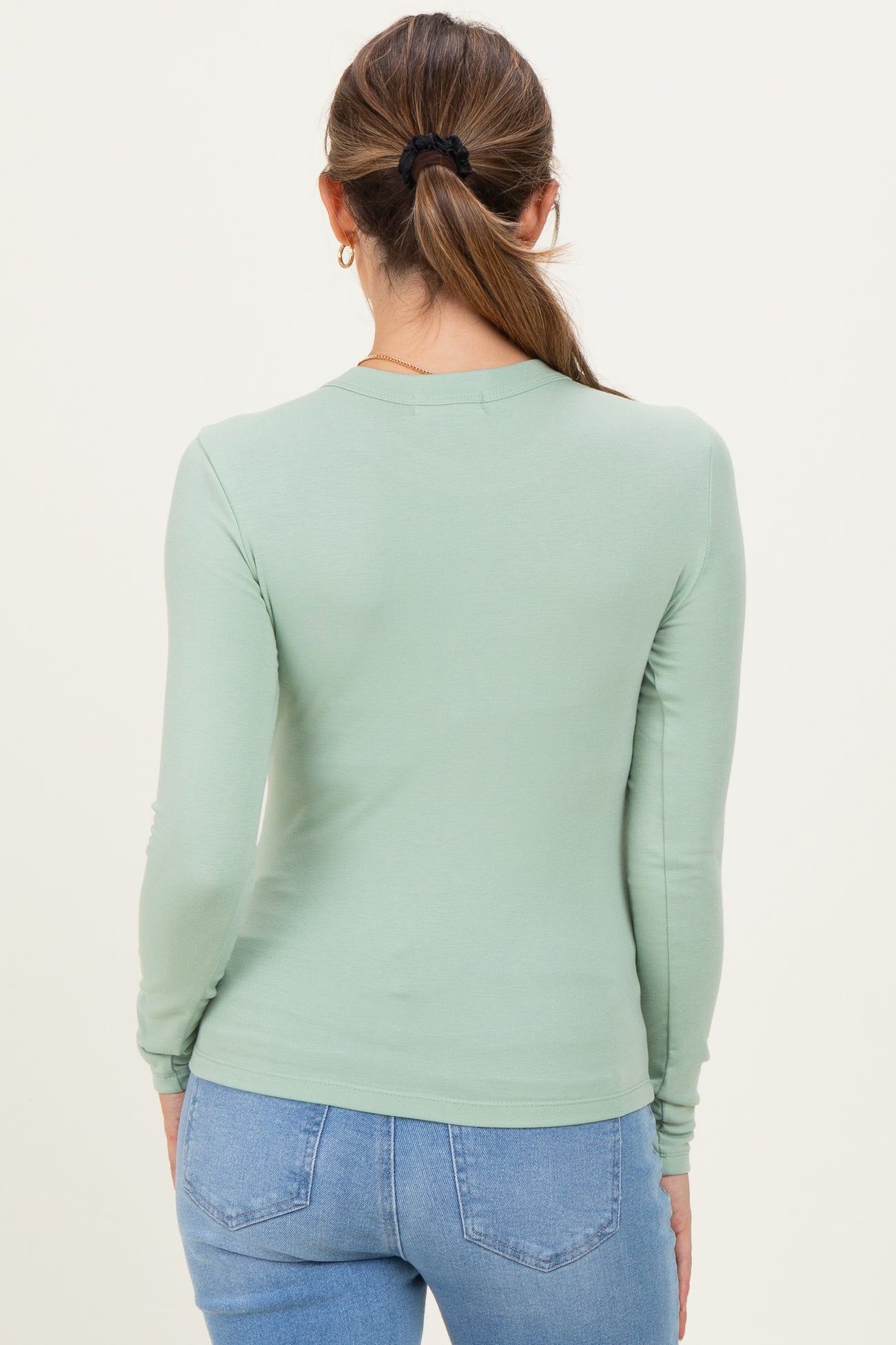 woman wearing a light green long sleeve maternity top viewed from the back with jeans