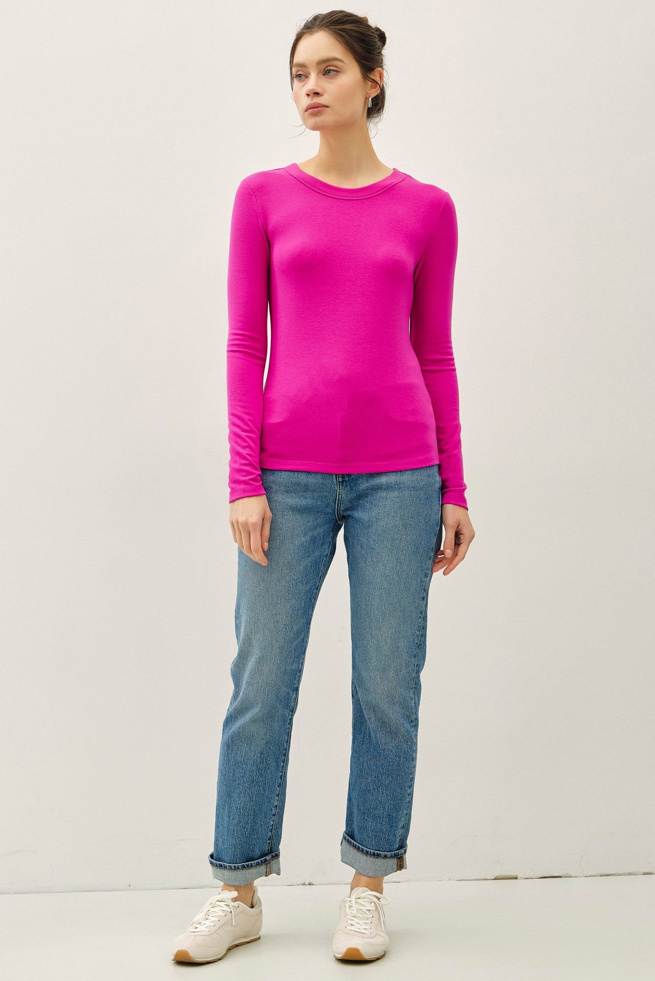woman wearing a bright pink long sleeve top with a fitted silhouette and light blue rolled cuff jeans