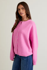 woman wearing a bright pink oversized cardigan with button closure and relaxed sleeves paired with blue jeans