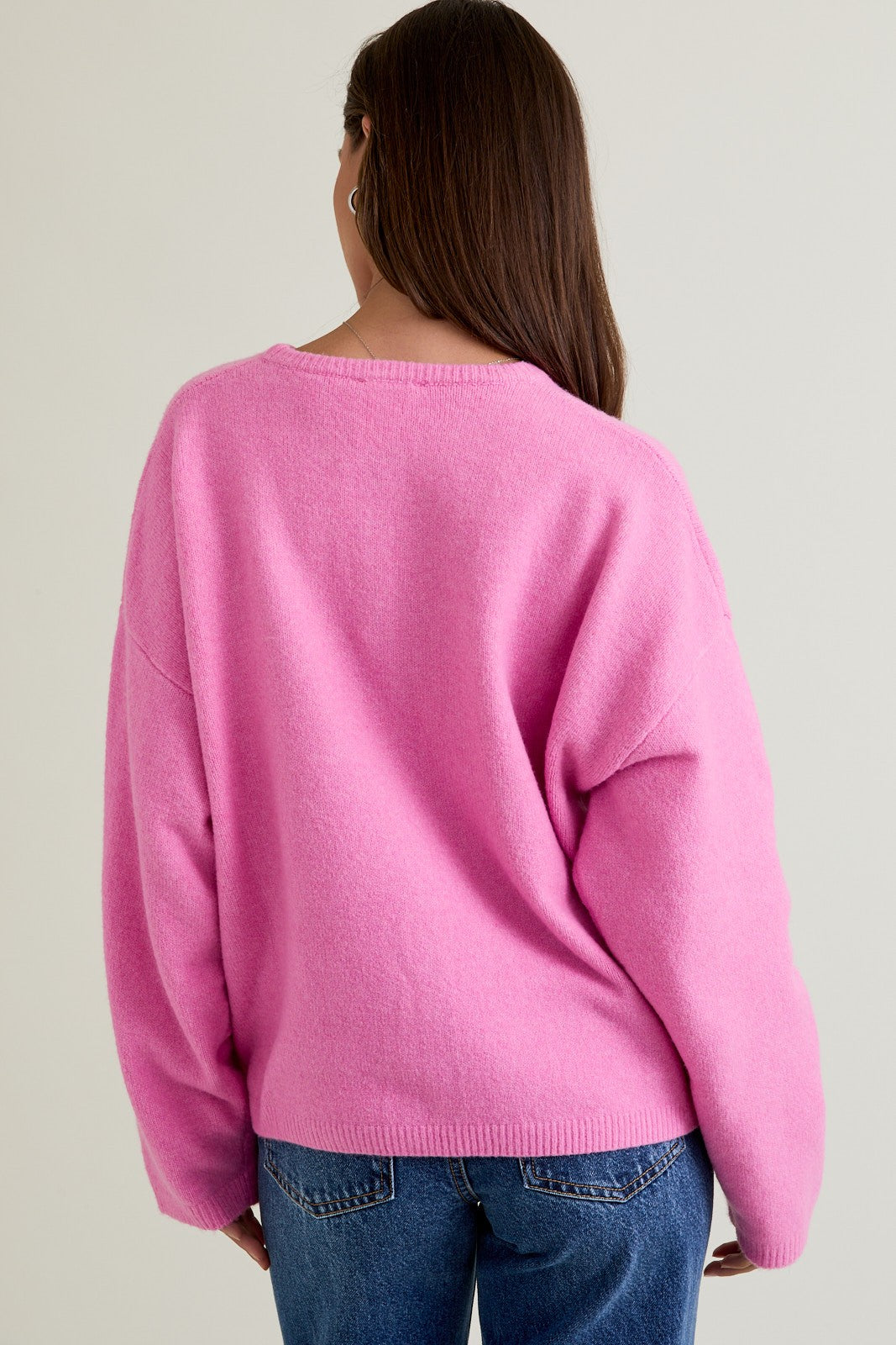 woman wearing a pink oversized sweater with a relaxed fit and back view, paired with blue jeans