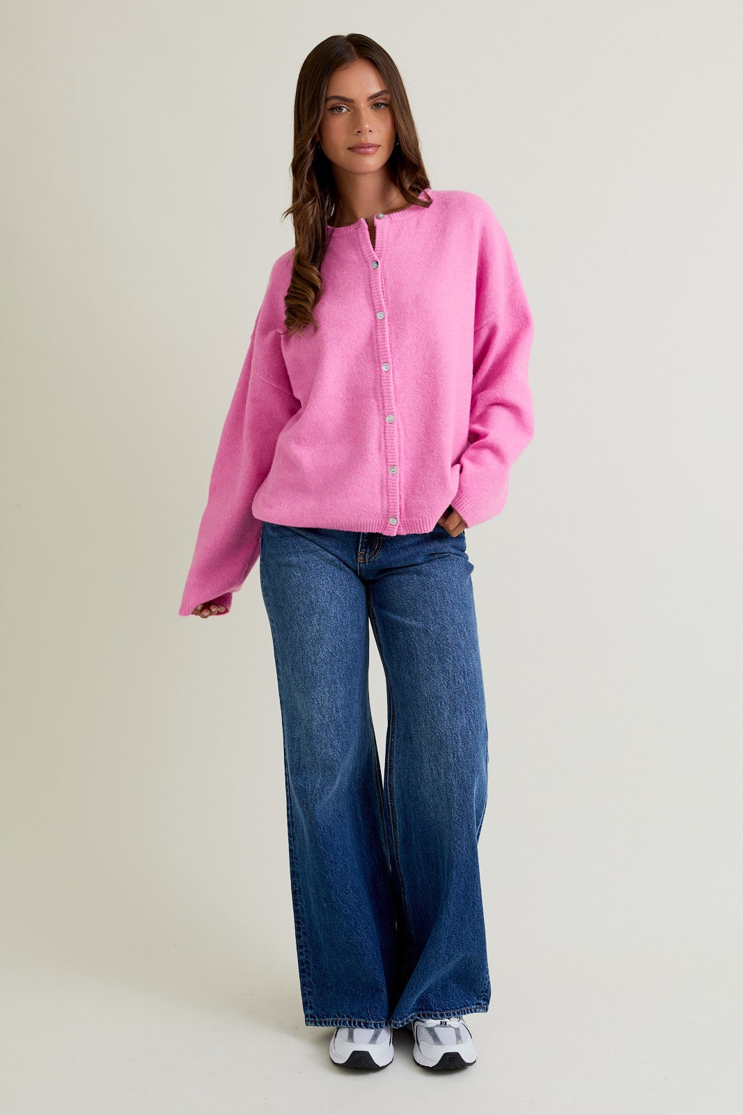 woman wearing a pink oversized cardigan with buttons and blue flared jeans, styled with sneakers