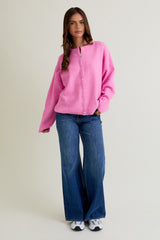 woman wearing a pink oversized cardigan with buttons and blue flared jeans, styled with sneakers