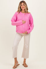 woman wearing a bright pink oversized cardigan and beige cropped pants, holding her baby bump