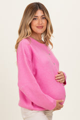 woman wearing a bright pink maternity sweater with buttons, holding her baby bump