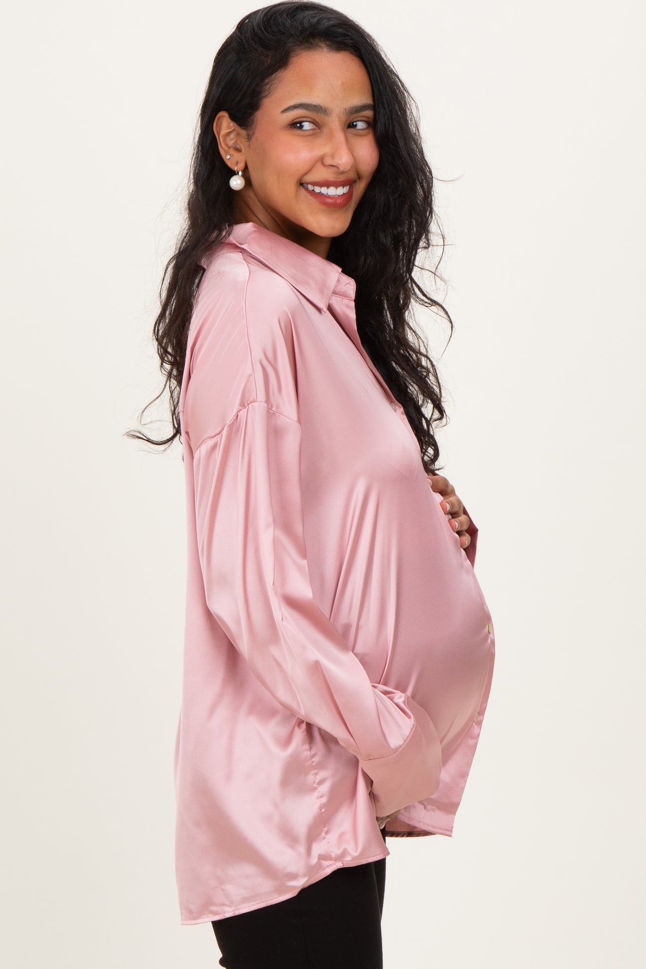 woman wearing a light pink satin long sleeve maternity shirt, smiling and showcasing her baby bump