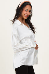 woman wearing a white satin maternity blouse and holding her baby bump, smiling with a headband on