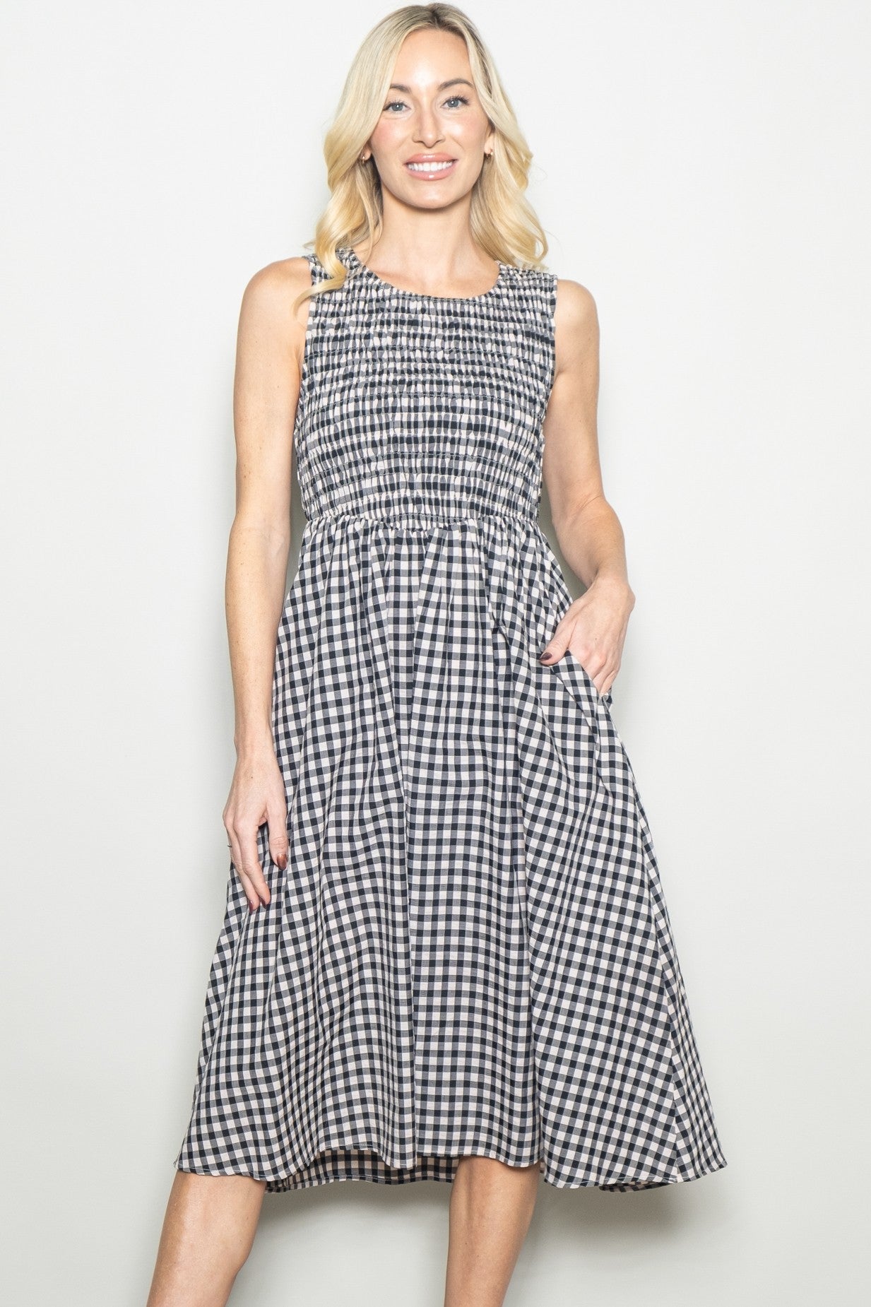 woman wearing a black and white gingham print sleeveless dress with a smocked bodice and pockets