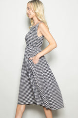 woman wearing a black and white gingham sleeveless midi dress with pockets, standing in profile