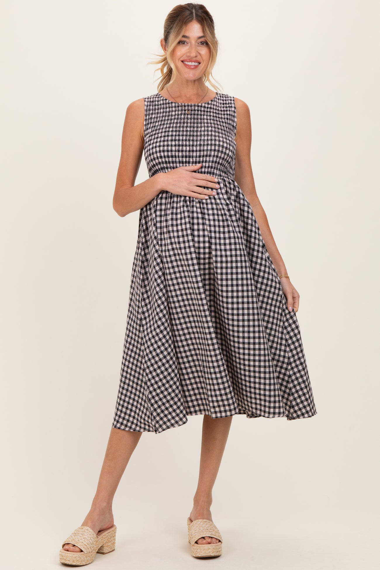 woman wearing a black and white gingham sleeveless maternity dress and holding her baby bump