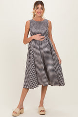 woman wearing a black and white gingham sleeveless maternity dress and holding her baby bump