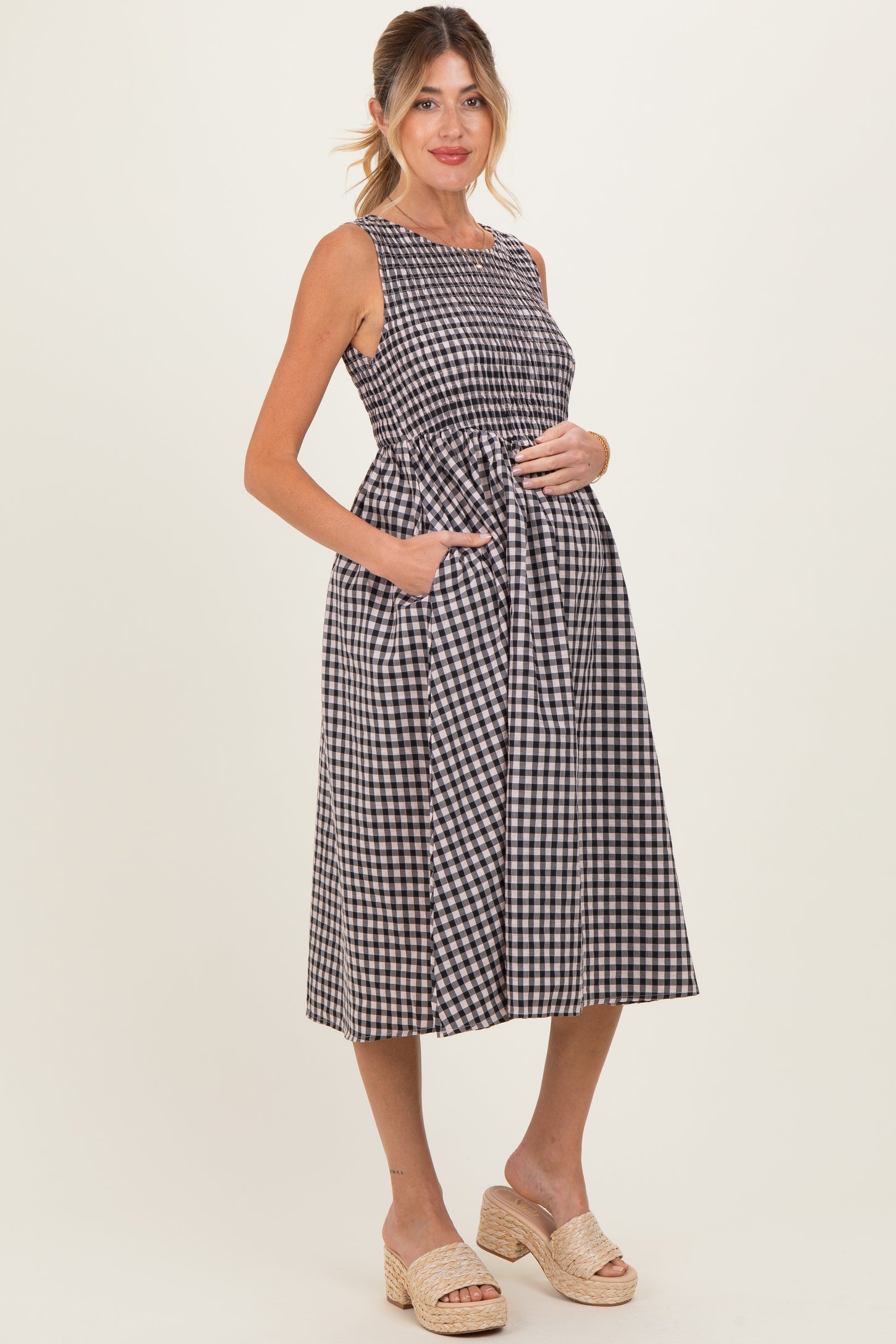 woman wearing a black and white gingham maternity dress with a tie waist and pockets, showcasing her baby bump