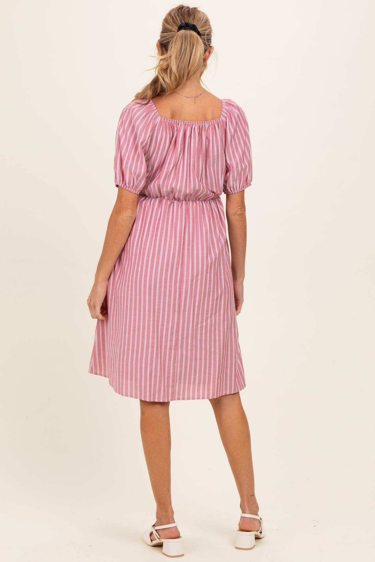woman wearing a pink and white striped maternity dress with puff sleeves and a gathered waist, seen from the back