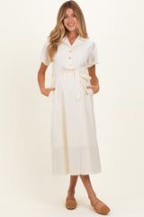 woman wearing a cream maternity dress with short sleeves, button details, and a waist tie, featuring side pockets