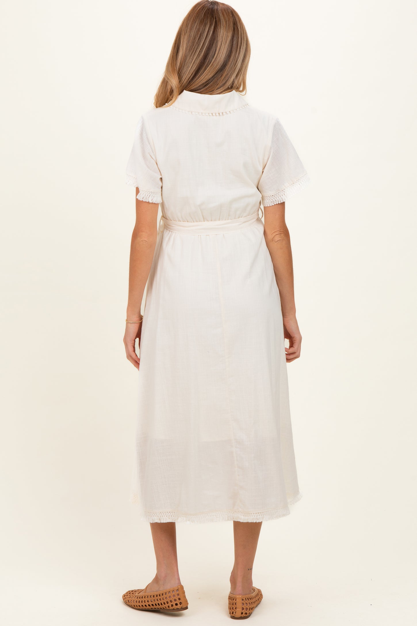 woman wearing a white maternity dress with short sleeves and lace trim, showing her back and styled with a tie belt