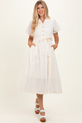 woman wearing a cream midi dress with short sleeves, button detail, tie waist, and pockets