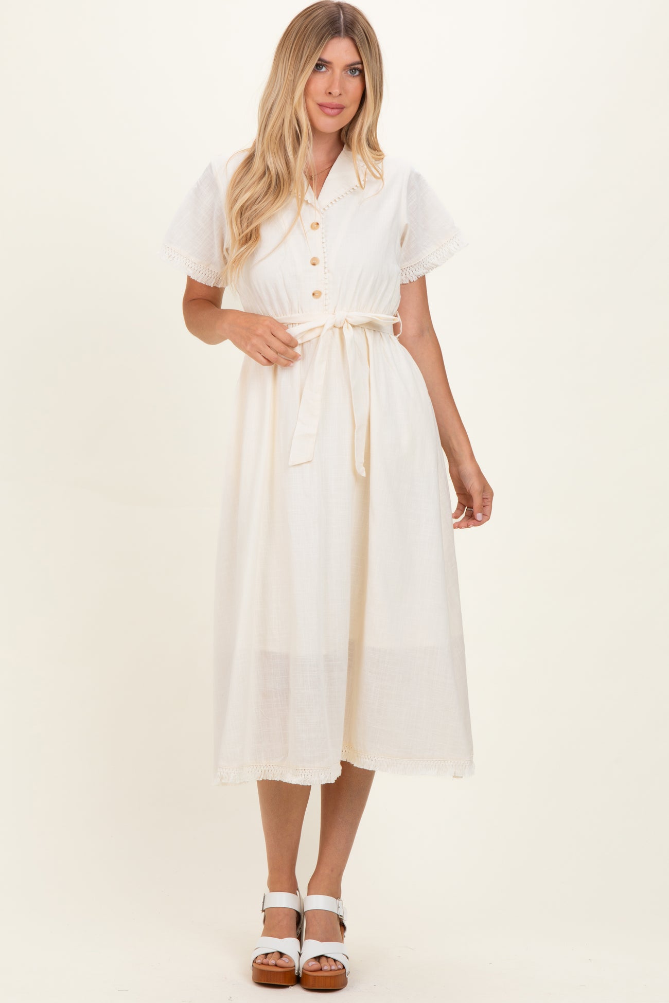 woman wearing a cream-colored midi dress with a button-up front, short sleeves, and a tie waist detail