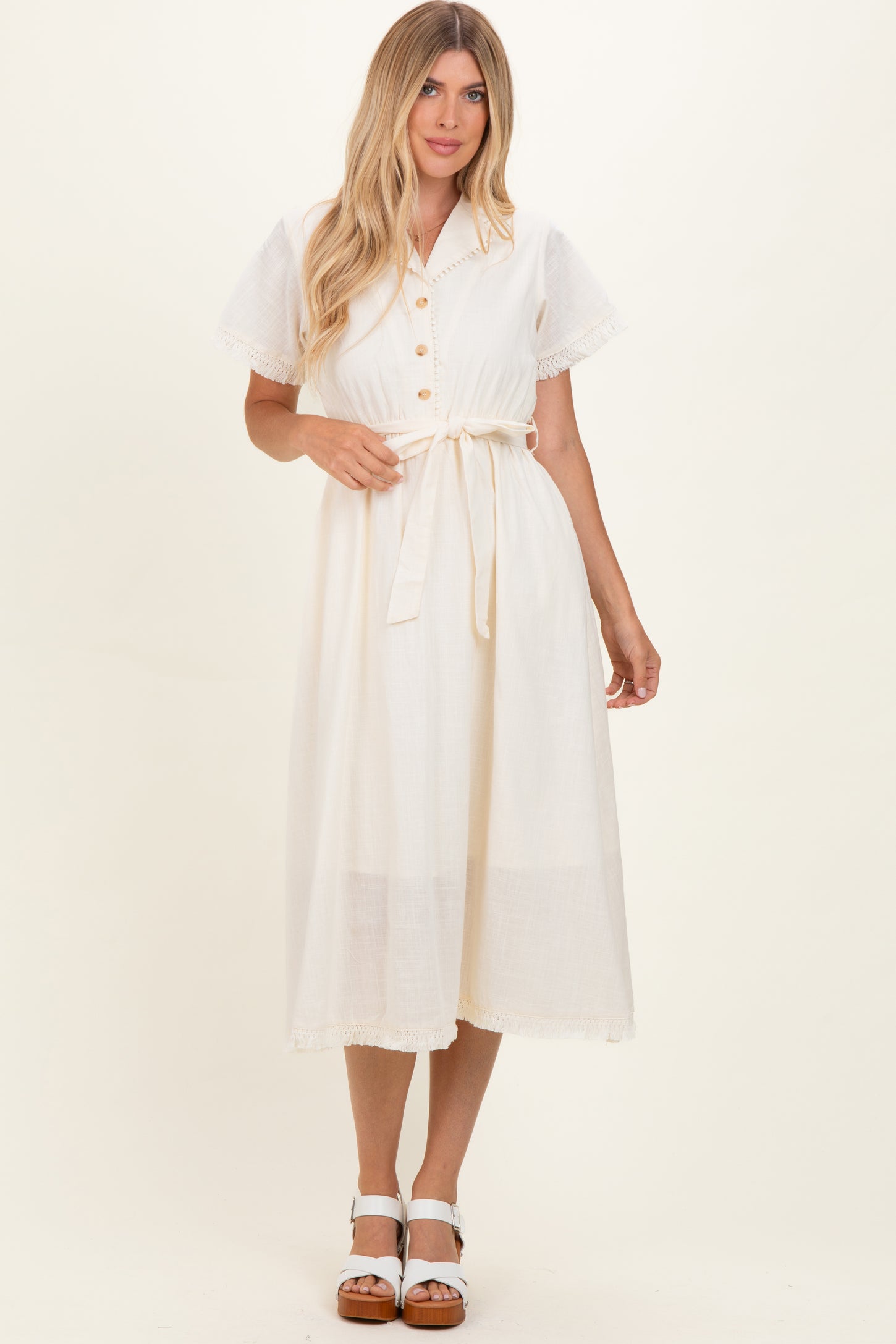 woman wearing a cream-colored midi dress with a button-up front, short sleeves, and a tie waist detail