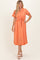 woman wearing a coral midi shirt dress with short sleeves, a tie waist, and fringe detailing at the hem