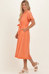 woman wearing an orange short sleeve midi dress with a tie waist and pockets