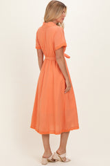 woman wearing an orange midi dress with short sleeves, a tie waist, and lace trim details, seen from the back