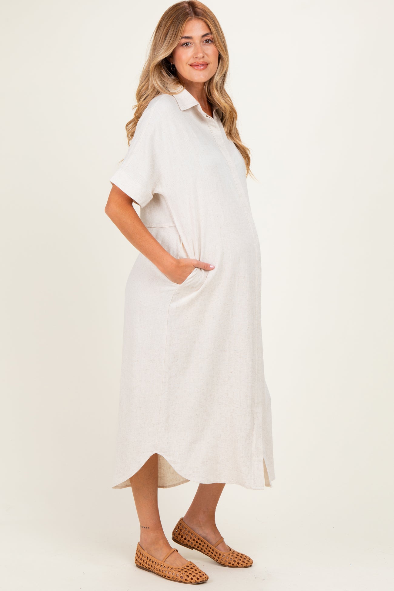 woman wearing a light beige maternity midi dress with short sleeves and pockets, showing her baby bump