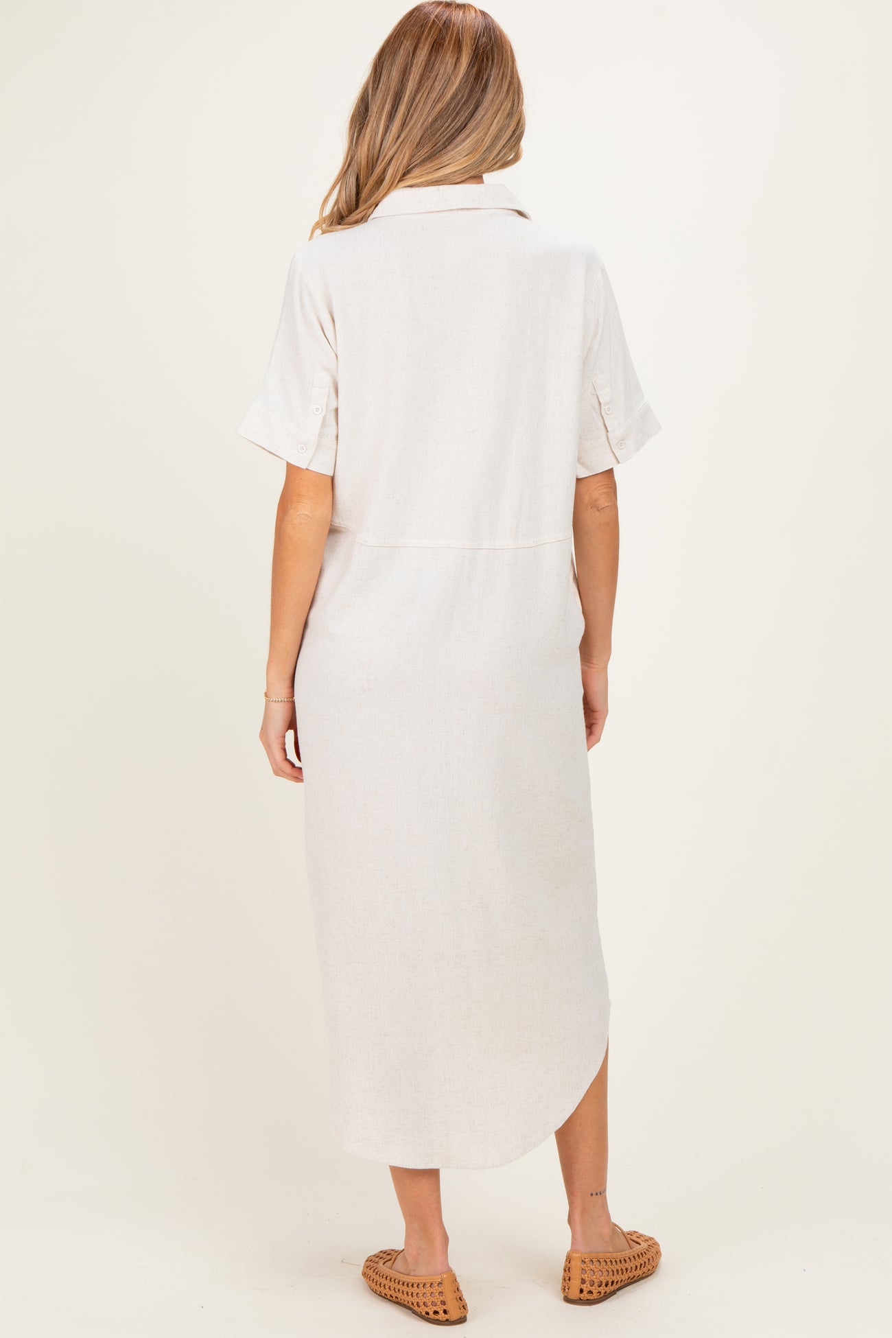 woman wearing a light beige maternity dress with short sleeves and a slightly curved hem, viewed from the back