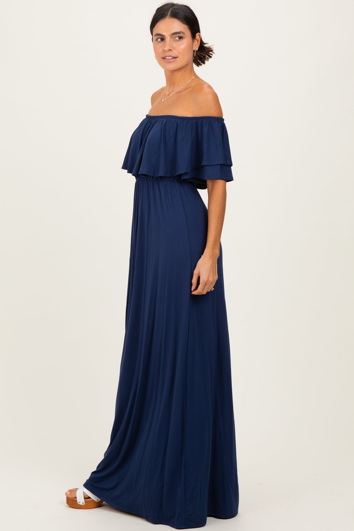 woman wearing a navy blue off-the-shoulder maxi dress with ruffle detail and a cinched waist