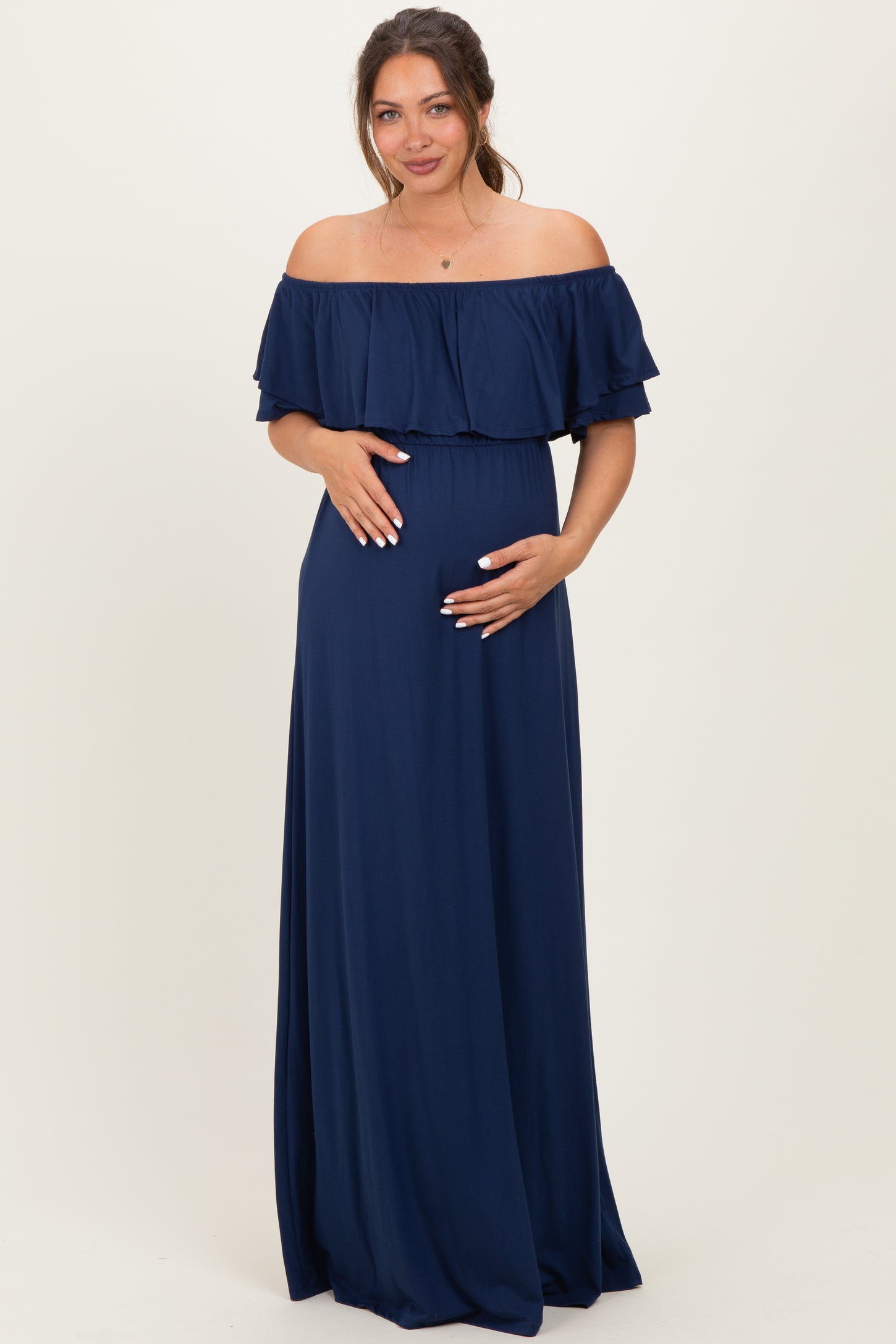 woman wearing a navy off-shoulder maternity dress with ruffle details and holding her baby bump