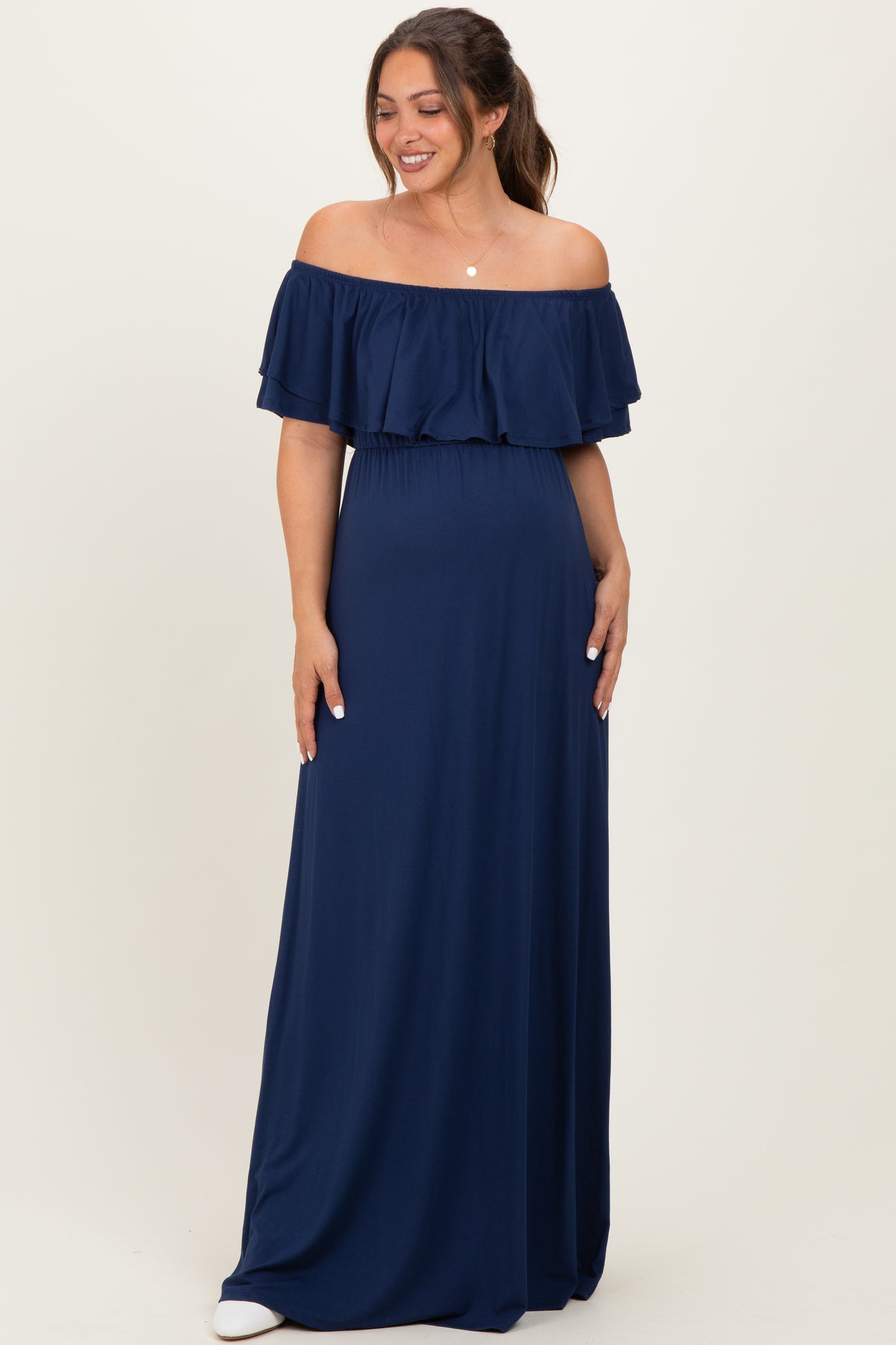 woman wearing a navy blue off-shoulder maternity maxi dress with ruffled sleeves and a relaxed fit, showing her baby bump