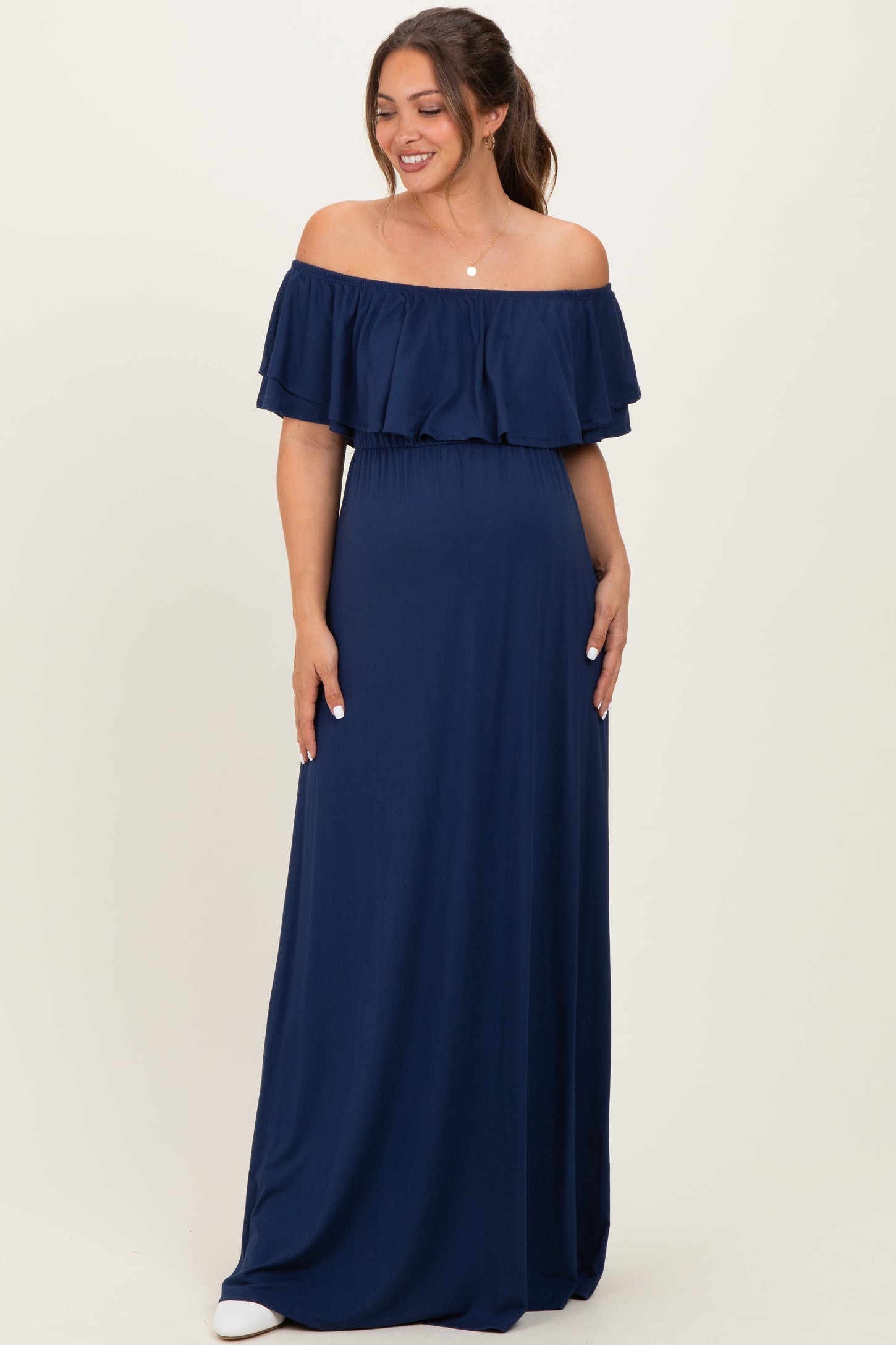 woman wearing a navy blue off-shoulder maternity maxi dress with ruffled sleeves and a relaxed fit, showing her baby bump
