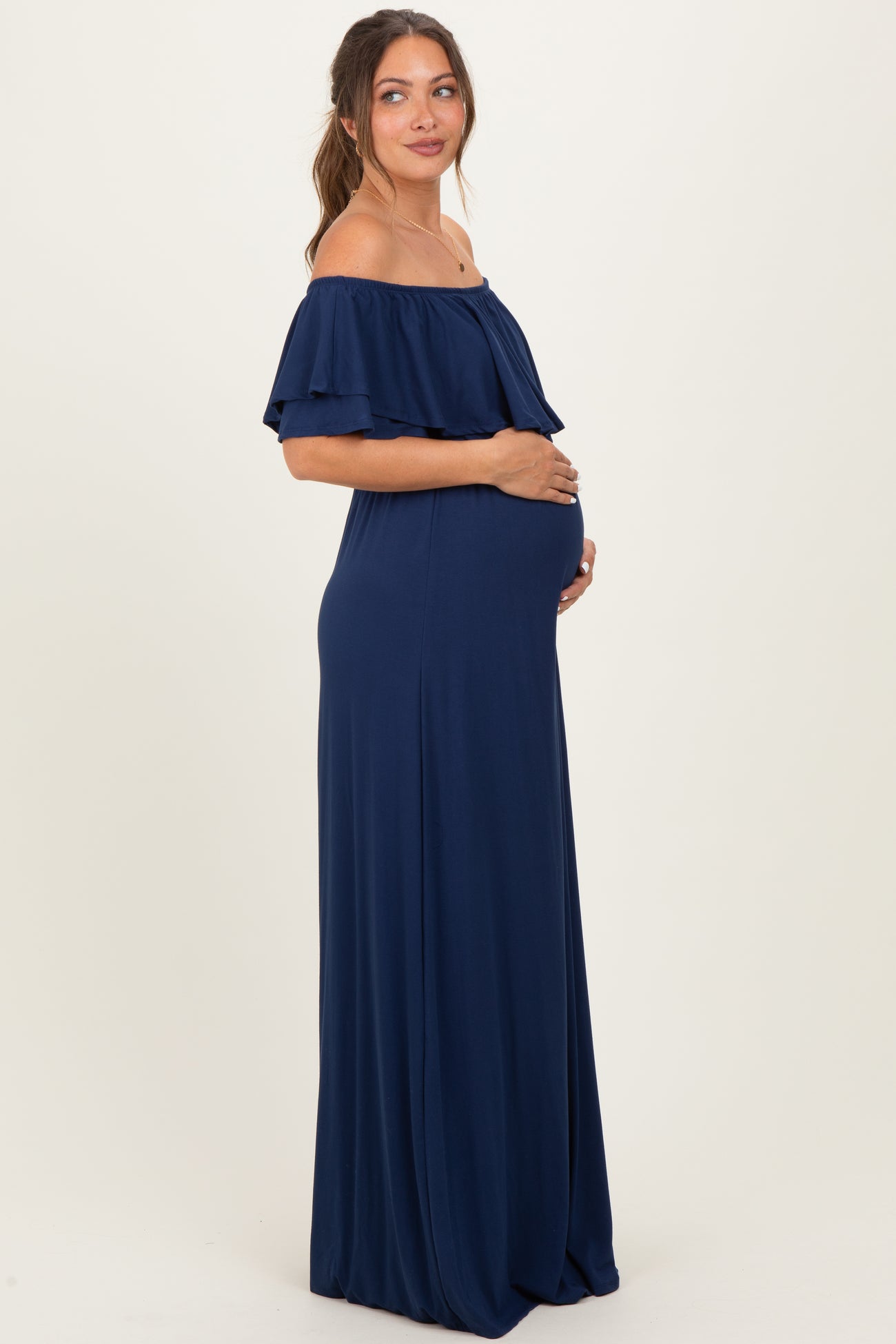 woman wearing a navy blue off-the-shoulder maternity dress, cradling her baby bump