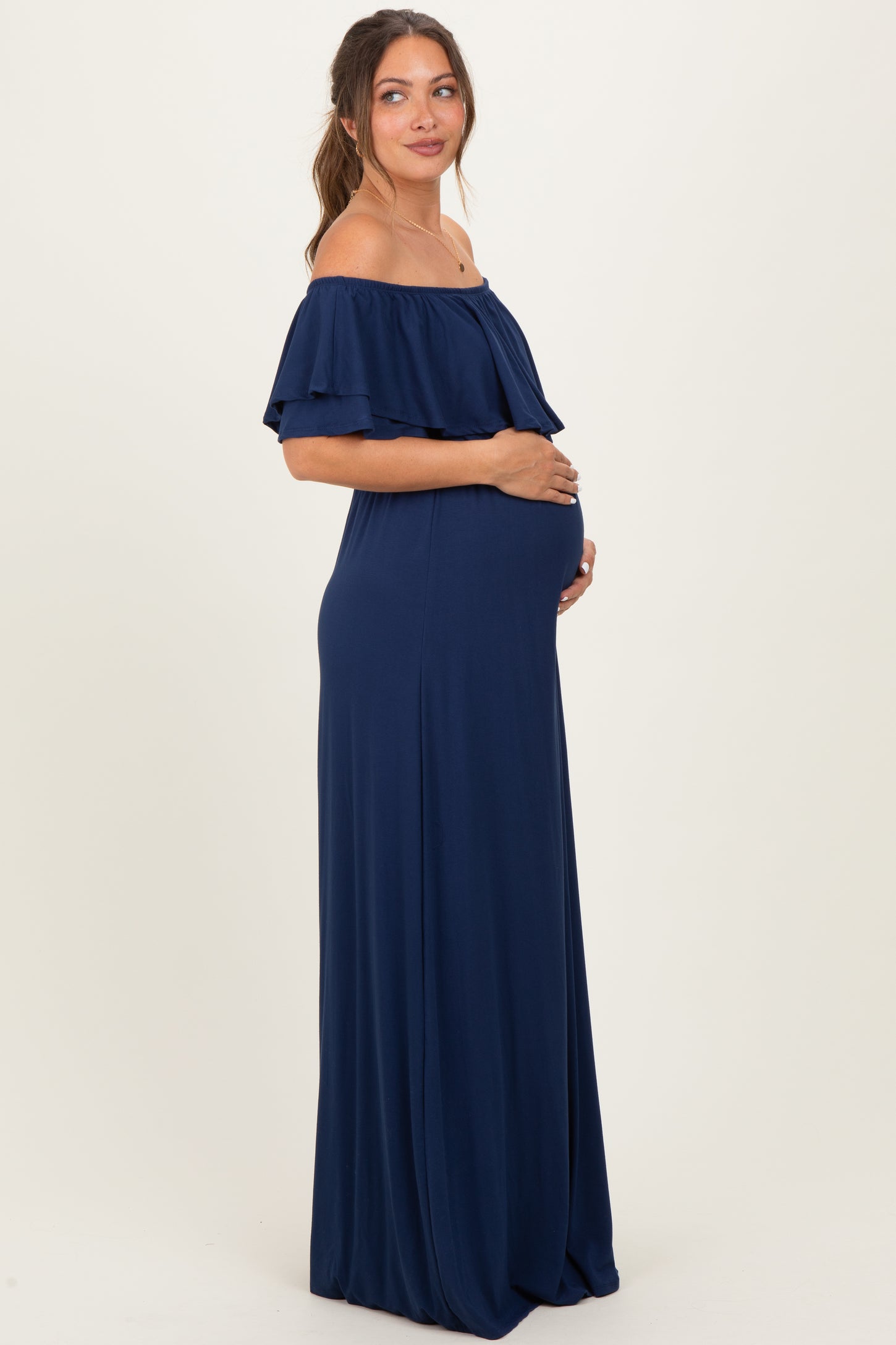 woman wearing a navy blue off-the-shoulder maternity dress, cradling her baby bump