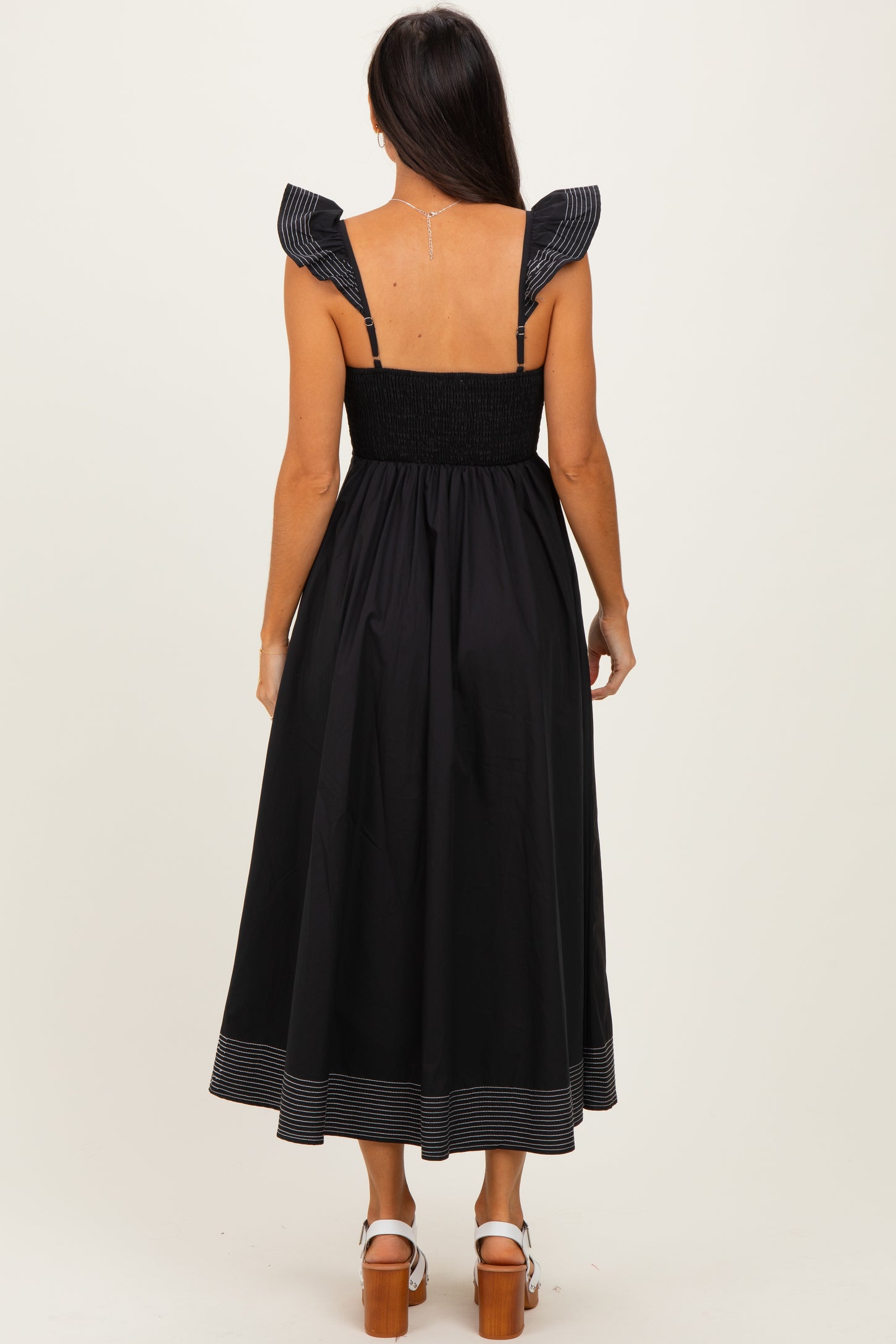 woman wearing a black midi dress with ruffled straps and striped hem, shown from the back