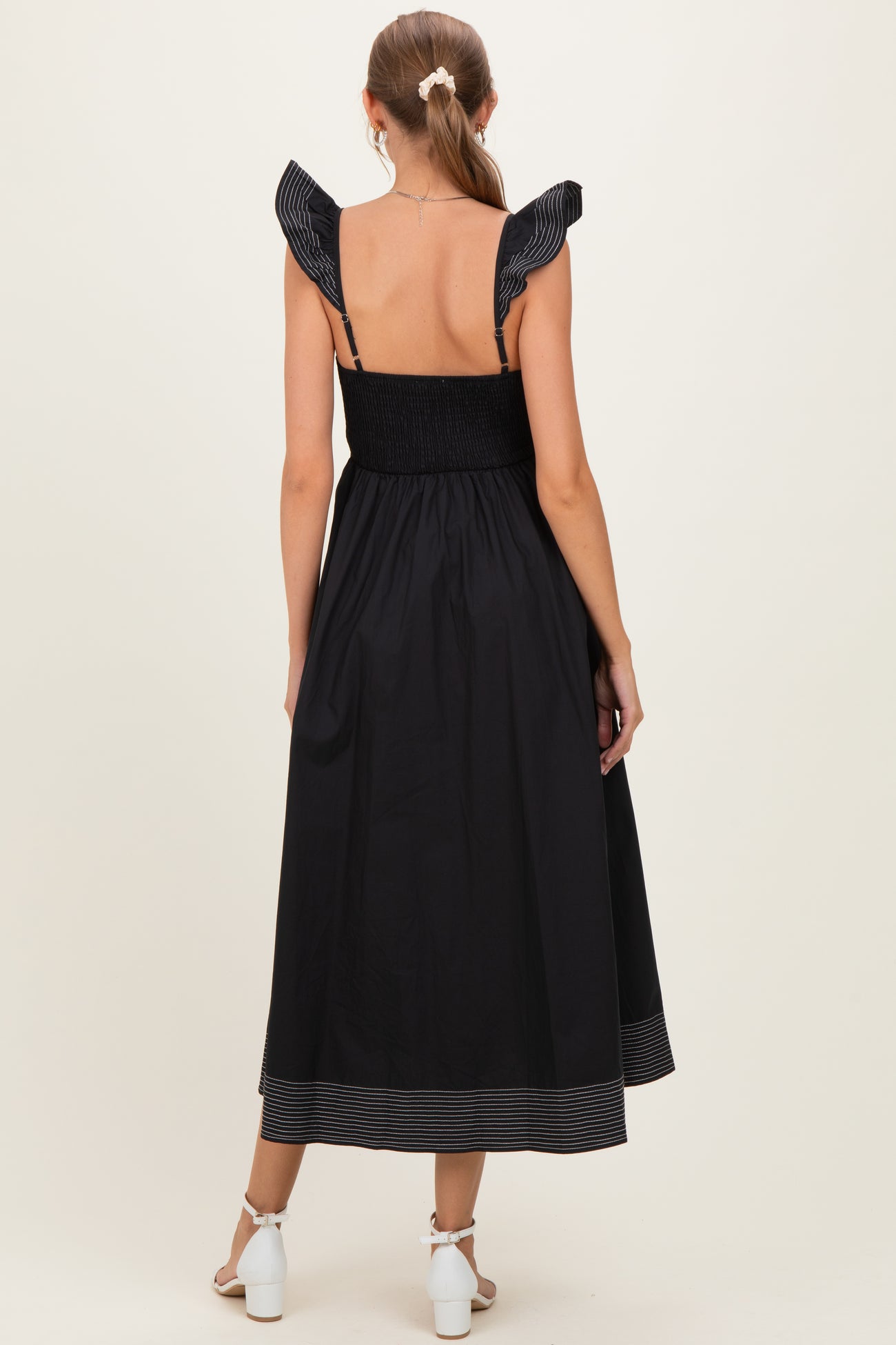 woman wearing a black maternity dress with ruffled shoulder straps and a smocked bodice, showing off a baby bump