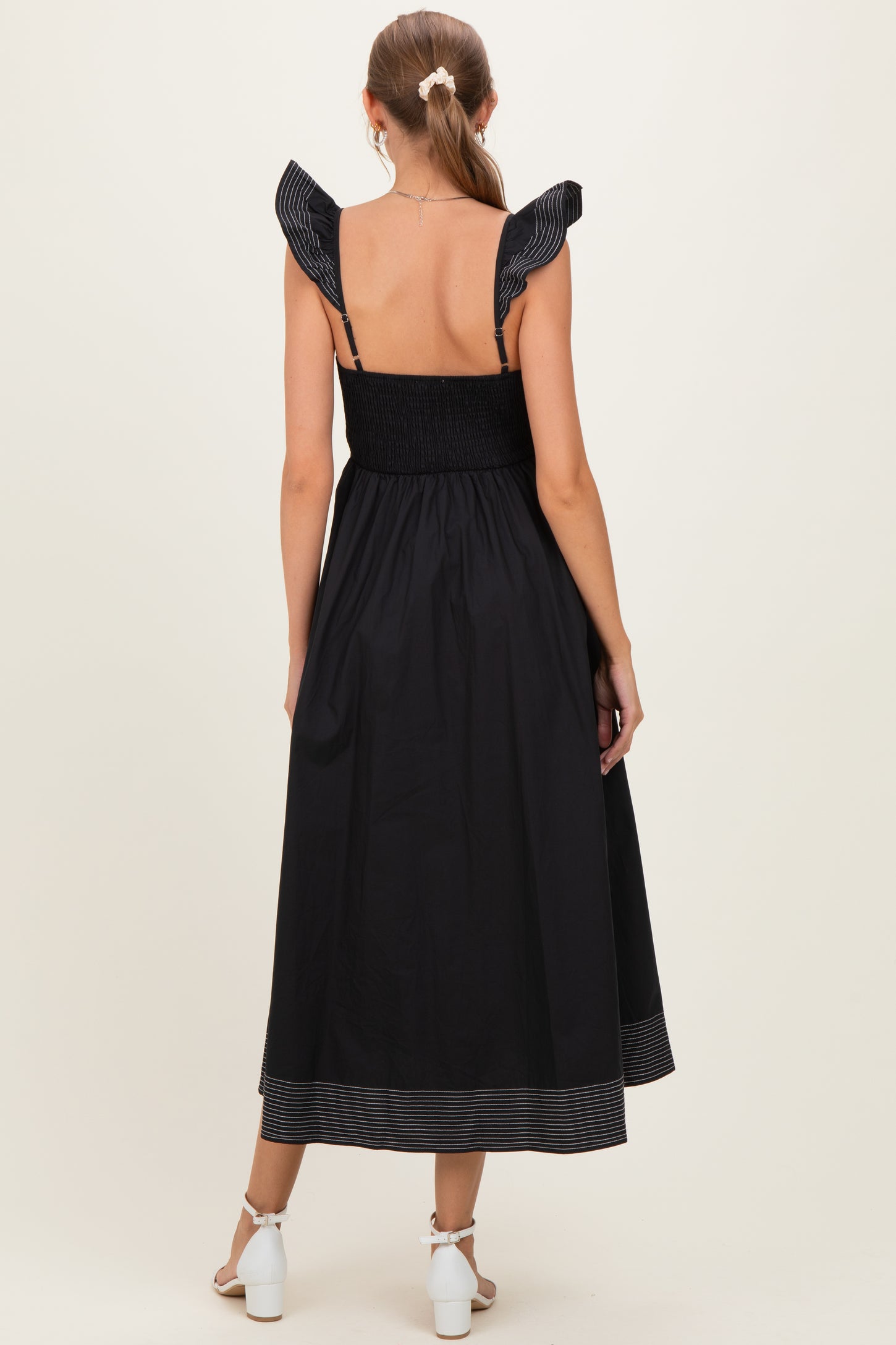 woman wearing a black maternity dress with ruffled shoulder straps and a smocked bodice, showing off a baby bump