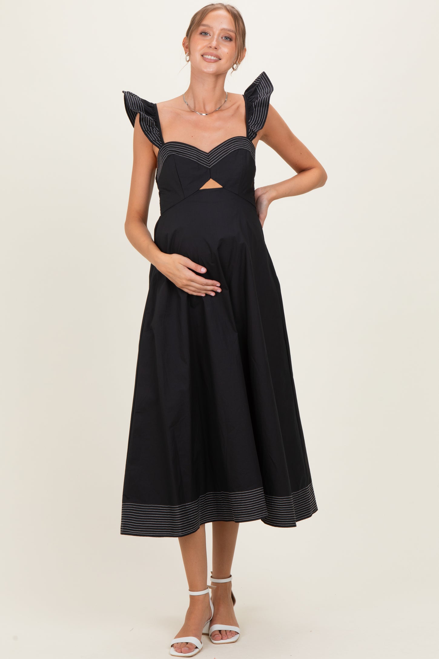 woman wearing a black maternity dress with ruffled straps and a cutout detail, holding her baby bump