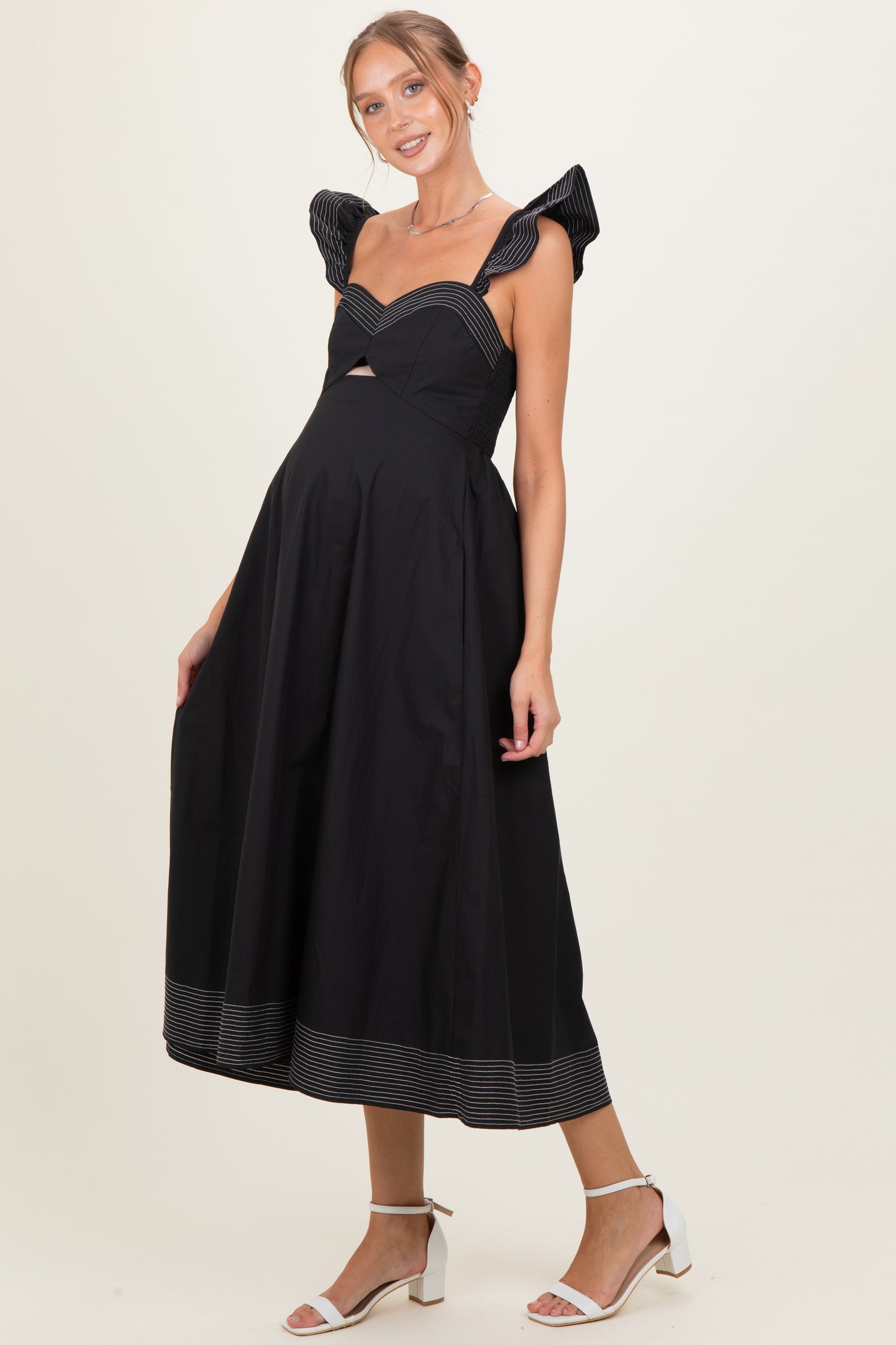woman wearing a black maternity dress with cut-out details and striped ruffle sleeves, showcasing her baby bump