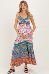 woman wearing a floral print maternity maxi dress with green and orange accents and holding her baby bump