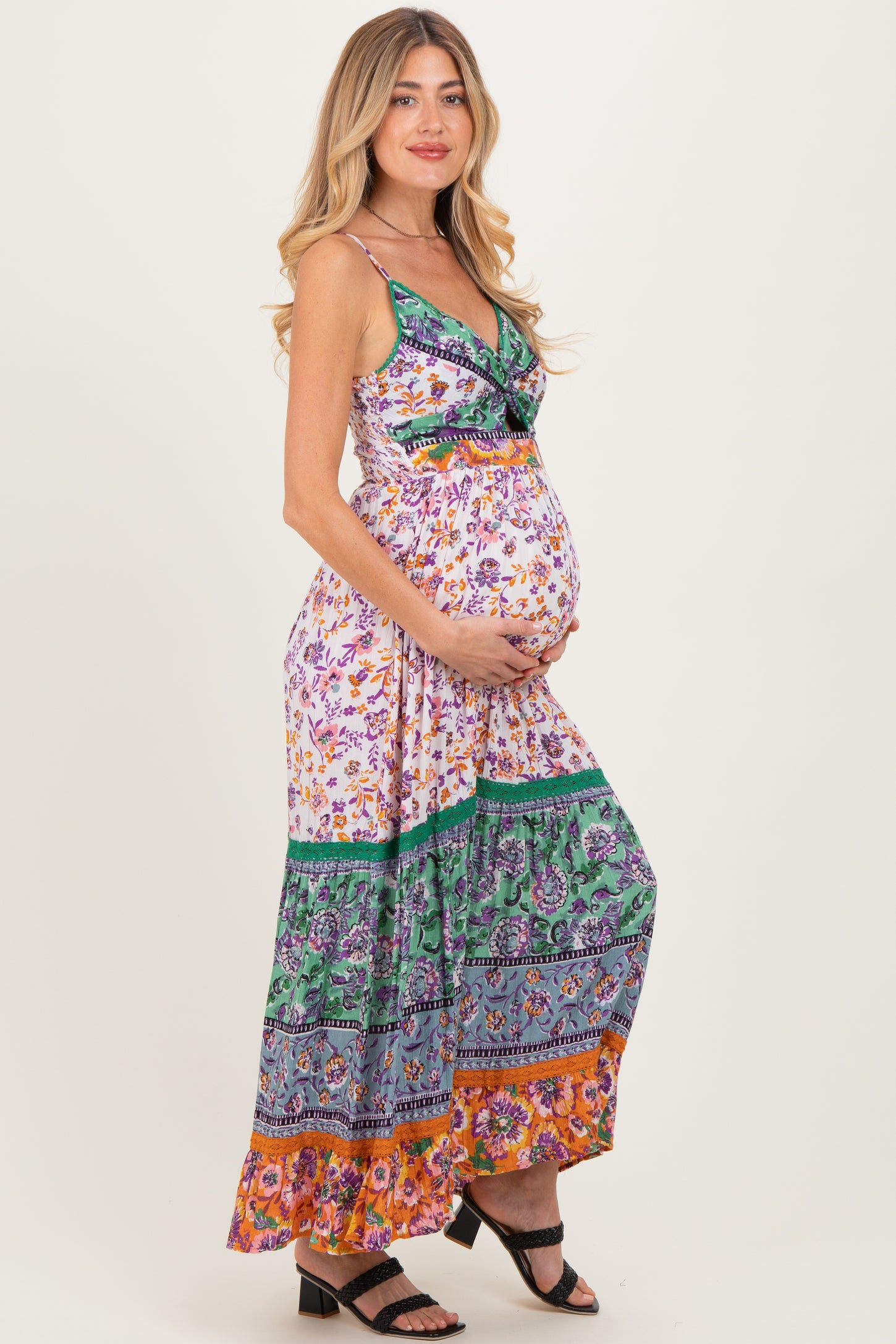 woman wearing a floral maxi maternity dress with a colorful hem and holding her baby bump