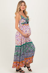 woman wearing a floral maxi maternity dress with a colorful hem and holding her baby bump