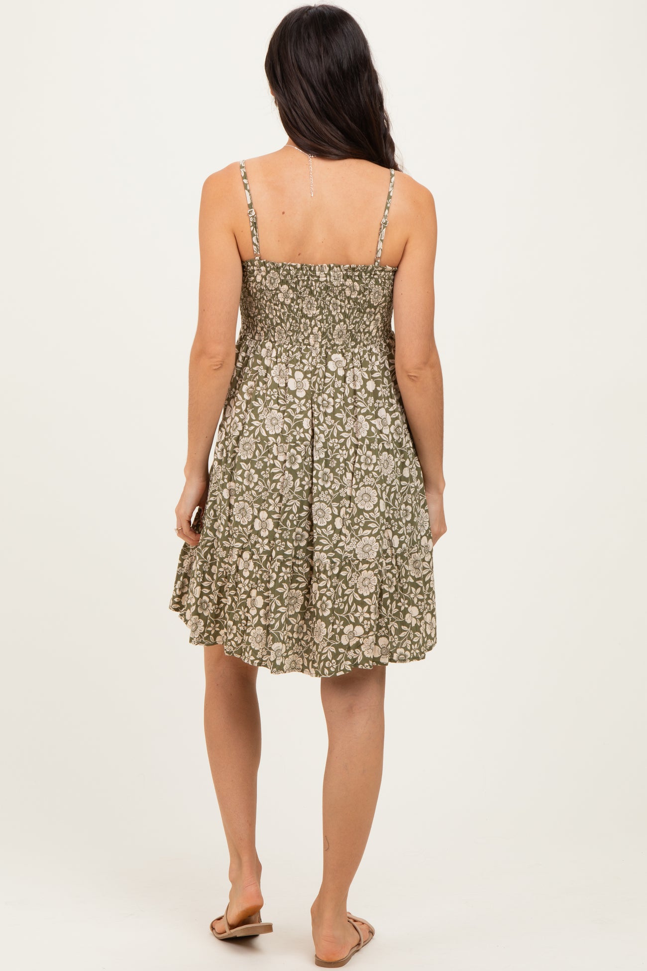 woman wearing a back view of a green floral print sundress with spaghetti straps and a flowy silhouette