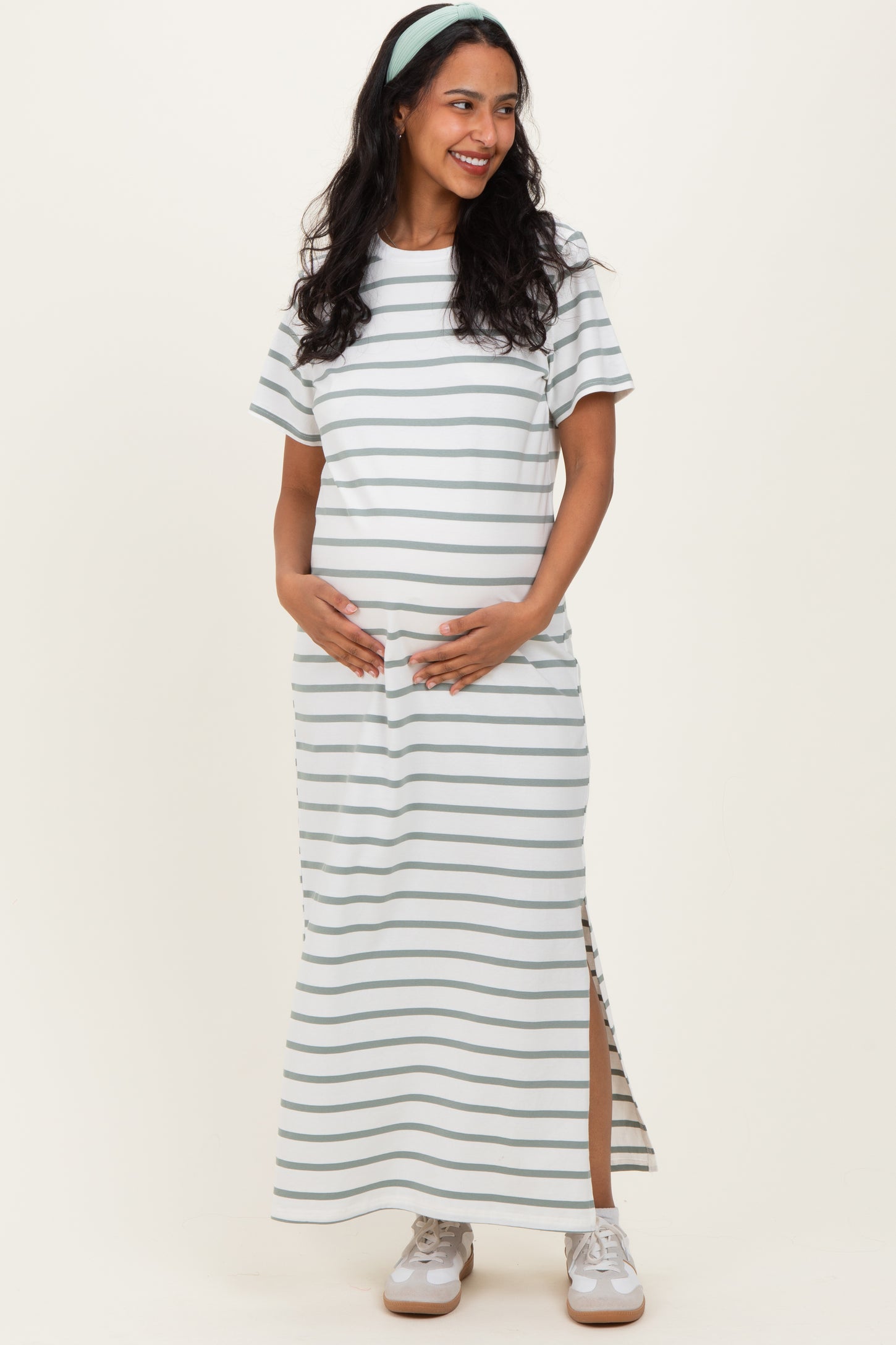 woman wearing a striped maternity maxi dress with short sleeves and side slits, gently cradling her baby bump
