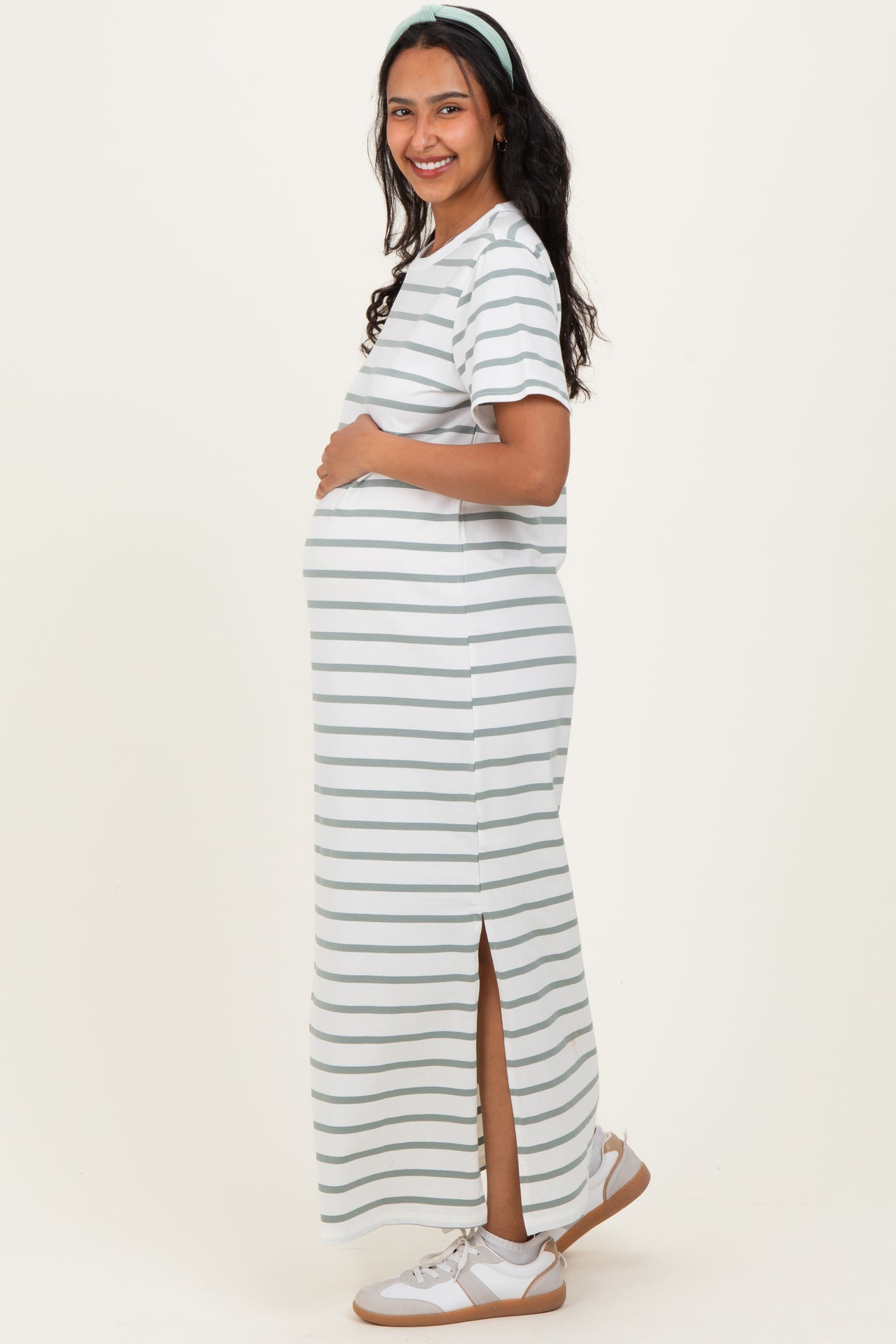 woman wearing a striped gray and white maternity maxi dress with side slits and holding her baby bump