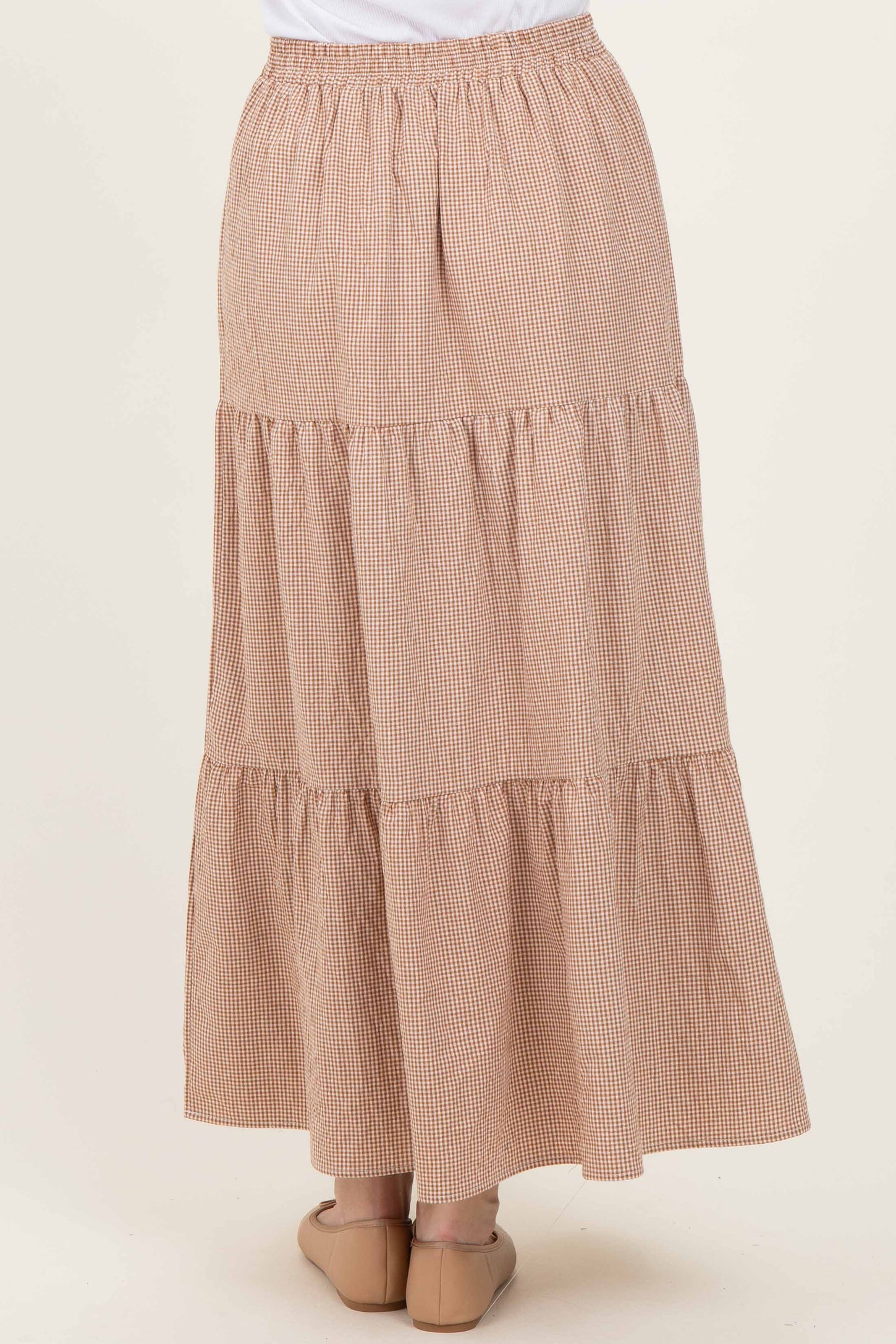 woman wearing a tiered maxi skirt in a brown and cream checked pattern, featuring an elastic waistband and flowing style