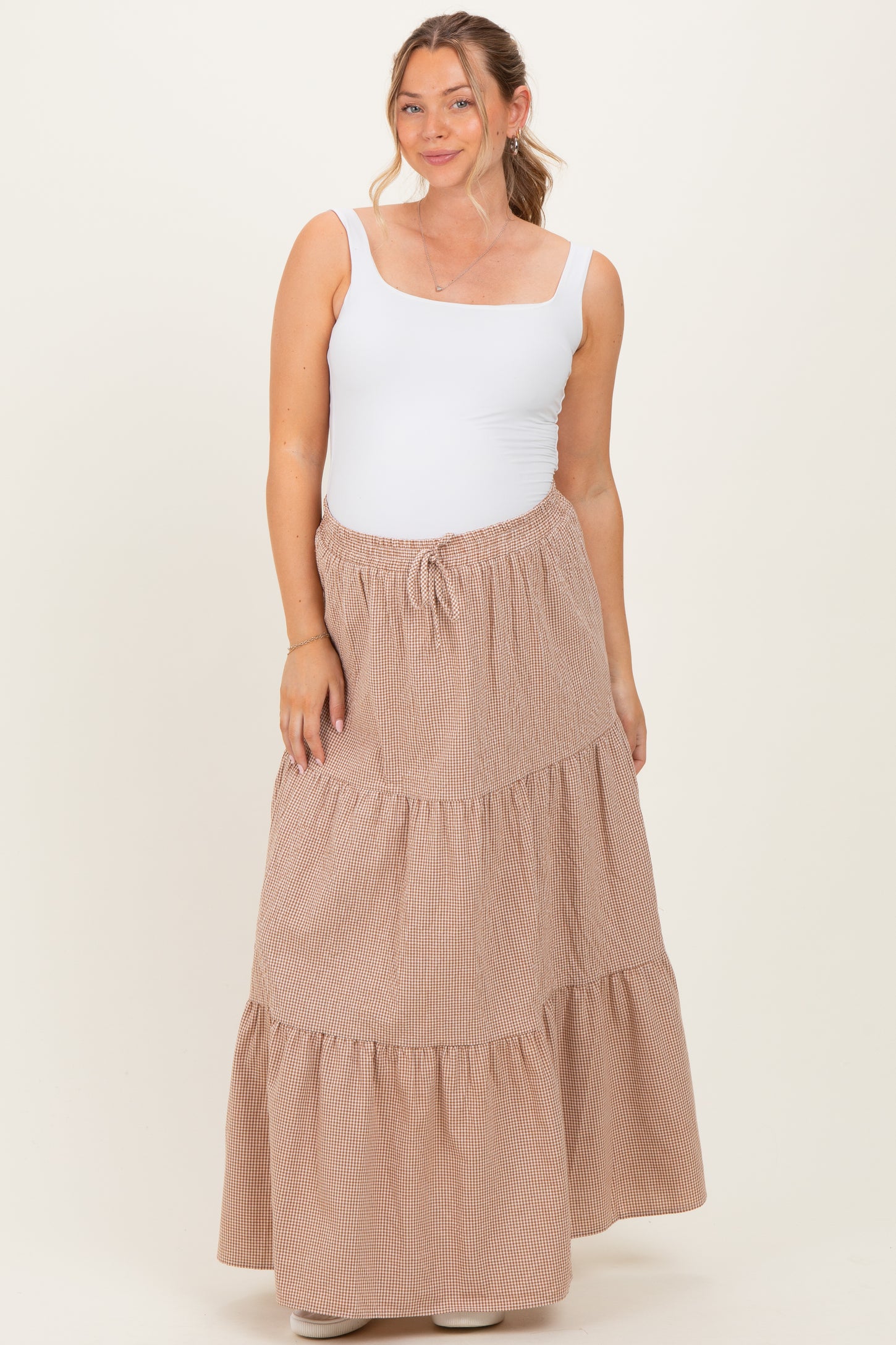 woman wearing a white tank top and a beige striped maternity maxi skirt with a tiered design and drawstring waist