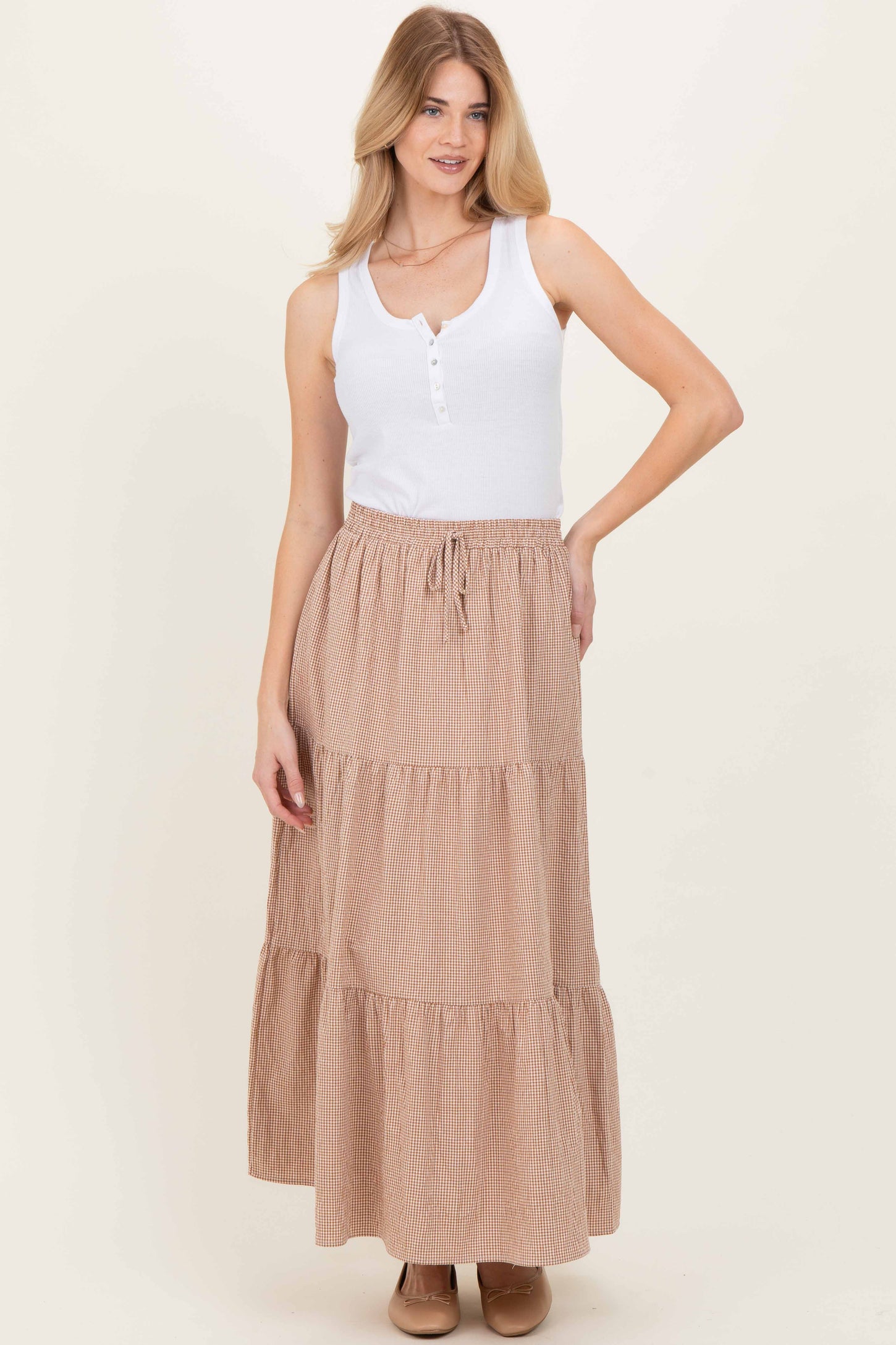 woman wearing a white sleeveless henley top and a tan striped maxi skirt with tiered layers