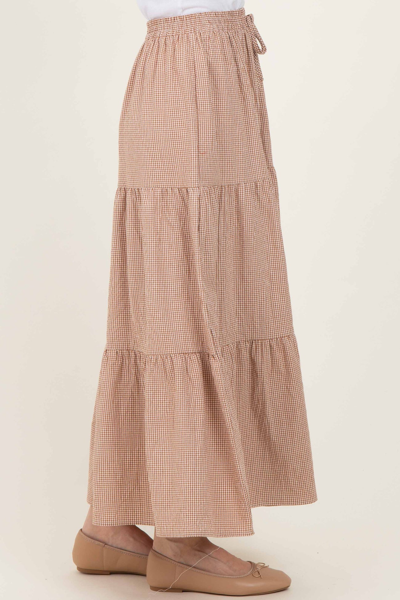 woman wearing a long brown gingham tiered maxi skirt with an elastic waistband and drawstring detail